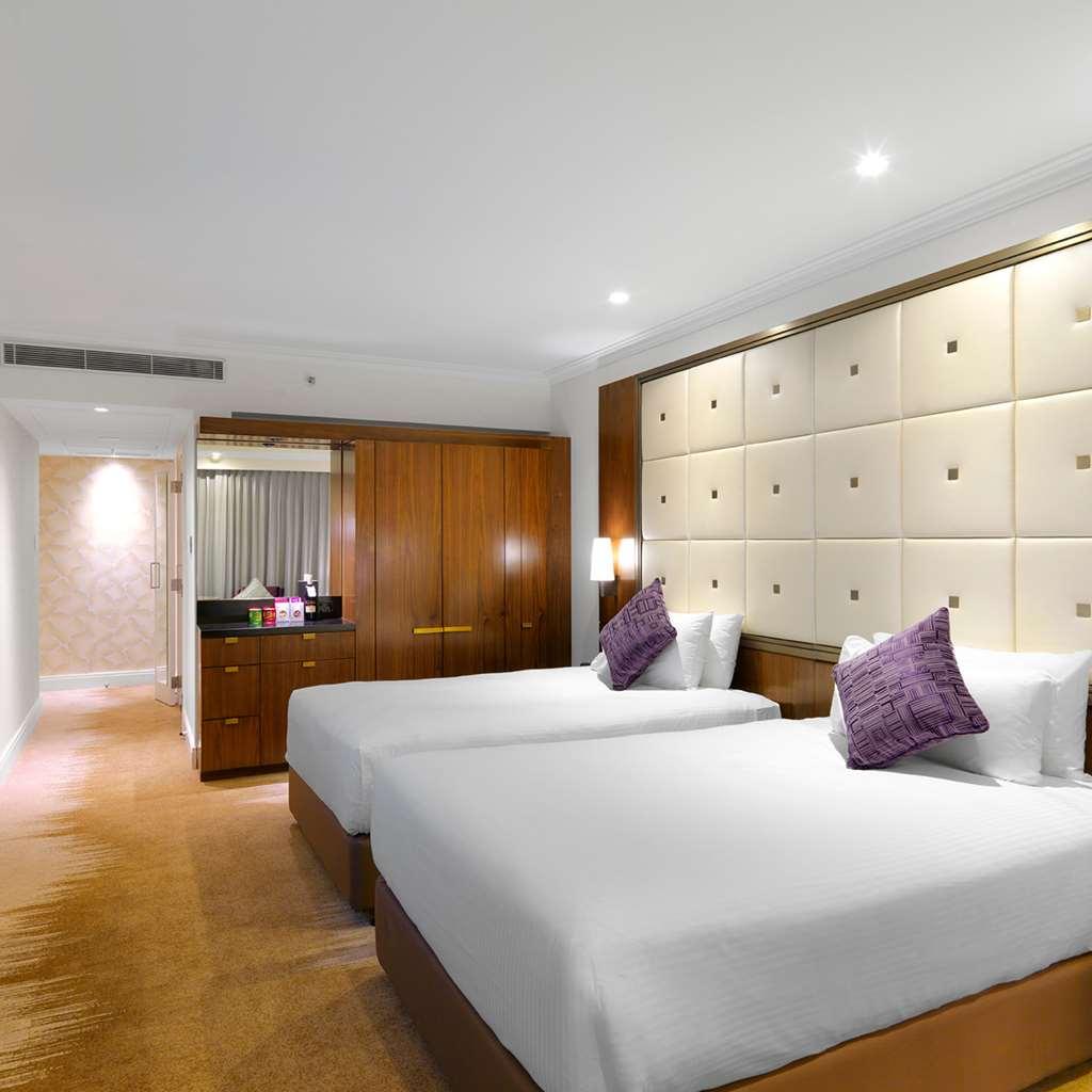 โรงแรมอโมร่า แจมิสัน ซิดนีย์ ห้อง รูปภาพ The photo shows a modern hotel room featuring two twin beds with white bedding and purple decorative pillows. The walls are designed with soft beige panels, creating a luxurious ambiance. There’s wooden furniture, including a cabinet against one wall